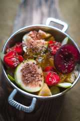 Bright fruit salad with figs and strawberries in a tin bowl on a wooden stand