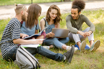 College friends sitting on lawn in campus, communicating. Young people in campus studying outdoors.