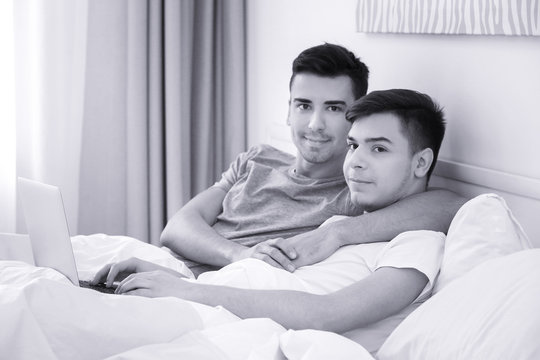 Happy gay couple lying in bed with laptop at home
