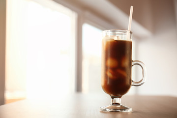 Glass cup of cold brew coffee and straw on light blurred background