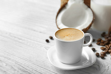 Cup of tasty coconut coffee, beans and nut on wooden table
