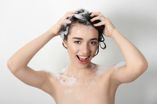 Young woman washing hair while taking shower on white background
