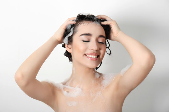 Young woman washing hair while taking shower on white background
