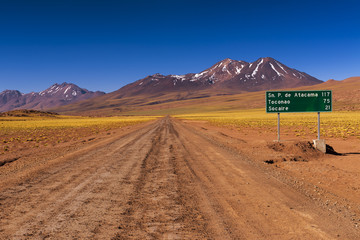 Dirt road with a road sign and mountains in the background, in the Atacama Desert, Chile; Concept for travel in Chile
