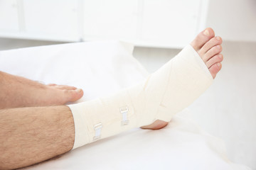 Young man with bandaged leg in clinic, closeup