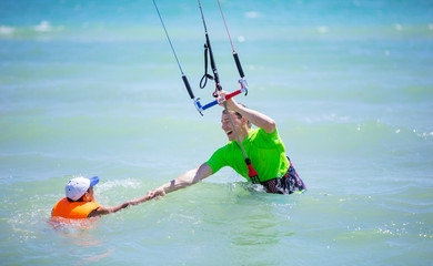 Male kite surfer helping young boy to come closer