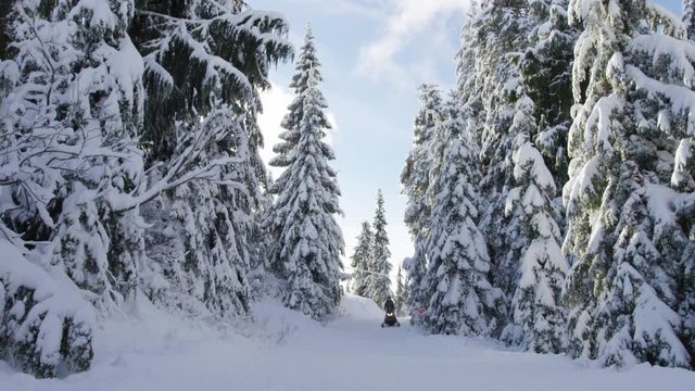 A snowmobiler waves as he drives by on a snowy mountain lane on Grouse Mountain near Vancouver, Canada. 4k. Slow motion.