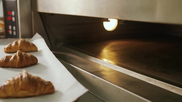 Close up shot of young man hands in the uniform taking beatiful fresh croissant from oven.
