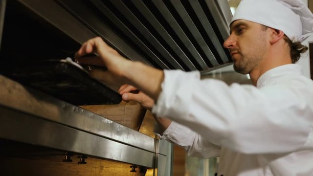 Portrait of young man in the uniform putting breads to the oven.