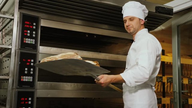 Young baker man taking beatiful fresh golden bread from the stylish modern oven and showing it to the camera.