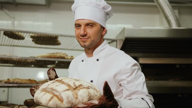 Portrait of smiling attractive worker in bakery shop with tasty bread possing on camera and smelling the fresh bread.