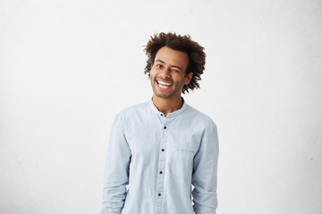 Indoor portrait of cheerful playful young Afro American man in good mood flirting, smiling broadly...