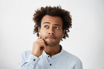 Close up portrait of forgetful and clueless dark-skinned student with stubble touching face, trying to recollect line while declaiming poem in front of class, looking away, primming up his lips