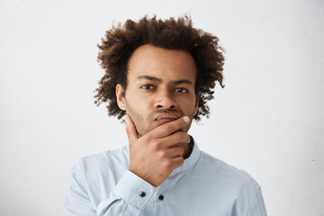Attractive young Afro American businessman touching face, having pensive indecisive look, feeling...