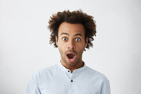 Body language. Headshot of attractive and surprised African American unshaven male student, staring at camera in full disbelief after he passed all exams with excellent marks, screaming Oh my God!