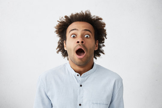 Omg, Wow. Picture of funny emotional dark-skinned male customer in light-blue shirt gaping with wide eyes, shocked with big sale prices on package tour holiday, feeling impatient and excited