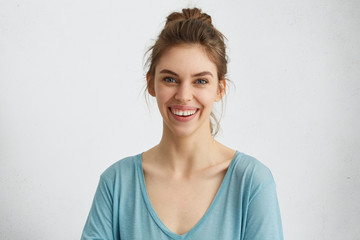 Happy smiling female with attractive appearance and dark hair tied in knot wearing blue blouse showing her broad smile having good mood liking to pose at camera. Happiness, positiveness concept