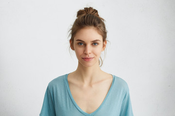 Portrait of beautiful female having blue shining eyes, thin lips, pure skin and dark hair tied in...
