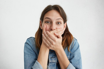 Beautiful brunette female bursting into laughing covering mouth with hands trying to stop her...