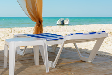 Wooden chaise longue, motorboat offshore in the sea