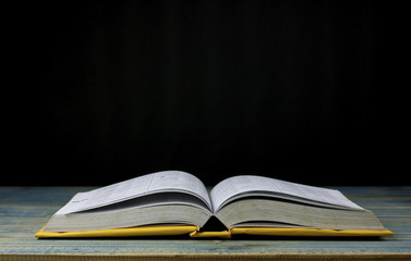 book on wood table and black  background, concept as opening paper will see knowledge of the world, learning by yourself and improve your life