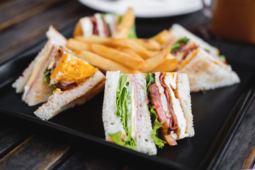 Slices sandwiches with french fried, on black dish, on wooden table, selective focus