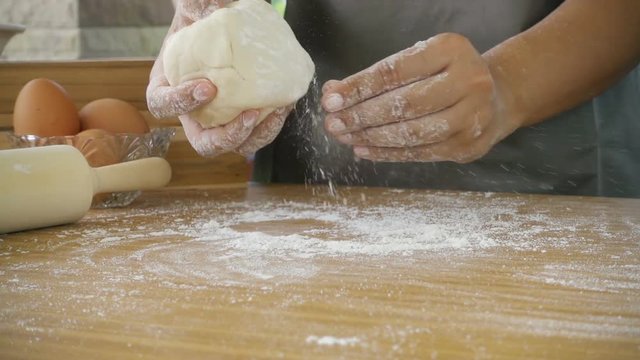 Female hand throwing flour on the table and kneading dough, slow motion