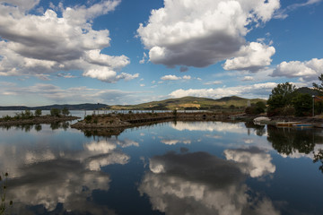A dock in a lake, with a beautiful, deep blue sky with white clouds reflecting on water