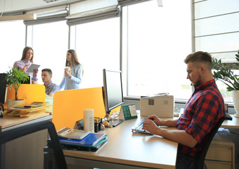 Fototapeta premium Handsome young man glasses holding smart phone and looking at it while sitting at his working place.