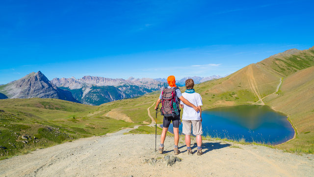 Couple of hiker on the mountain top looking at blue lake and mountain peaks. Summer adventures on the Alps. Wide angle view from above. © fabio lamanna