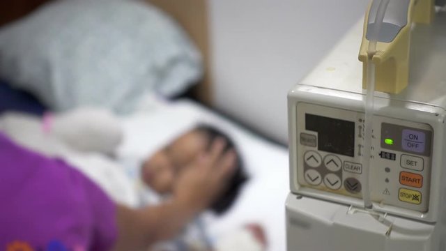 Closeup of female hand press switch on saline solution pump. Infusion pump with parent and sick little children blurred in the hospital.