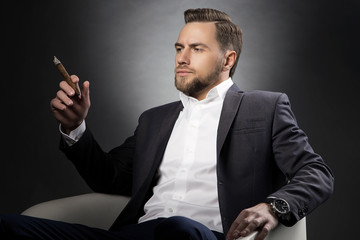 Portrait of ypung handsome man with perfect hair style and cigar wearing suit over dark background