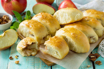 Homemade apple pies with fresh apples and walnuts from yeast dough on a kitchen wooden table. Apple patties on the table in a rustic style.