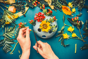 Female hand making autumn flowers  arrangements at blue florist workspace background, top view