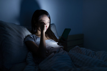 Woman feeling eye pain with using mobile phone on bed