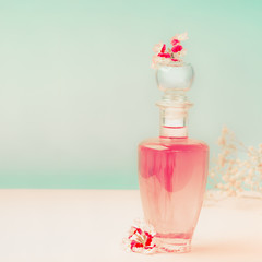 Pink Cosmetic bottle with skin care product or perfume with flowers Stands on the table at turquoise background, front view. Beauty concept