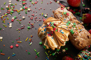 Delicious colourful eclairs with berries on dark stone background