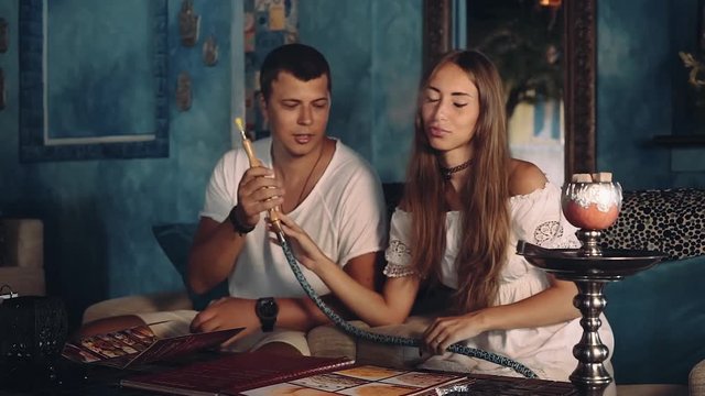 Young woman smoking shisha and passing it to man in shisha cafe, blue walls with ornament arabic style, camera slide. Shot with sony a7s on a slider