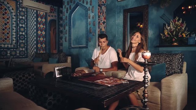 Happy european couple in arabic style shisha cafe, woman looking at menu while man is smoking, then she hugs him. Shot with sony a7s on a slider