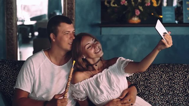 Young couple taking selfie sitting on a couch in shisha cafe, smiling. Shot with sony a7s on a tripod