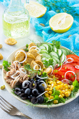 Salad with tuna, fresh tomato, cucumber, onion, pickled olives, corn and salad dressing vinaigrette on a gray stone background or slate.