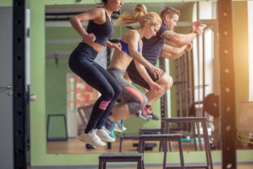 Male and female athletes doing box jumps at gym