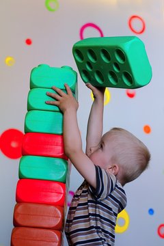 Child building a chimney from big colored cubes. Training moror skills.