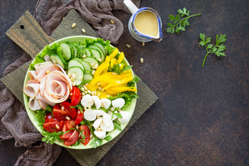 Summer Salad with vinaigrette salad dressing. Salad with ham, fresh vegetables, pine nuts and mozzarella on a gray stone background or slate. Top view. Copy space.