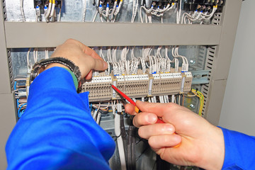 Engineer clamps electrical wires into terminals of electrical cabinet with screwdriver.
