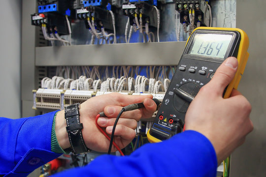 Electrician measures voltage with multimeter in  electrical cabinet.