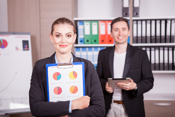 Portrait of beautiful bunsineswoman in office with her colleague in background. Corporate workers