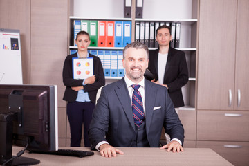 Senior businessman at the desk and his colleagues in the background. Business and finance