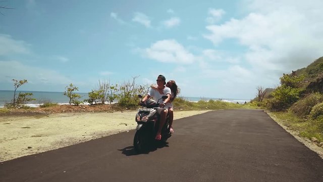 Couple riding motorbike on shore and between cliffs on a sunny summer day with blue sky, camera following, view from the front, Bali. Shot with sony a7s on a motorized 3-axis handheld gimbal.