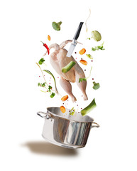 Flying raw chicken stock ,bouillon or soup ingredients with whole chicken, vegetables,seasoning, knife and cooking pot, front view, isolated on white background. Flying food concept